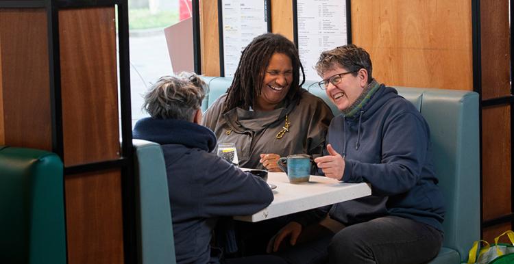 Three older woman sat in a booth in a cafe laughing