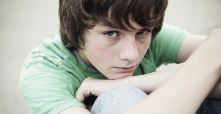 Young boy sitting down hugging his knees