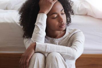 Young black woman sitting against bed with headache