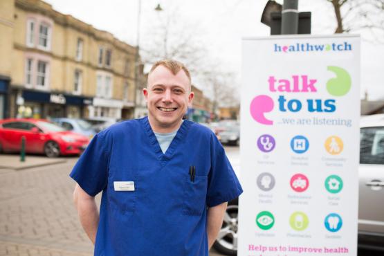 Male nurse standing in front of a Healthwatch sign that says 'have your say'.