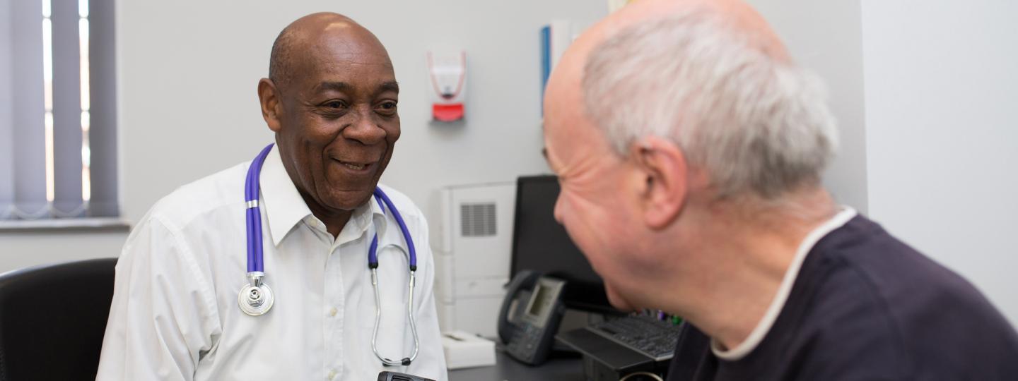 GP speaking to a patient, about to use a thermometer